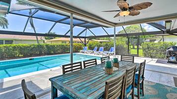 A covered outdoor area with a pool, lounge chairs, and a table with chairs.