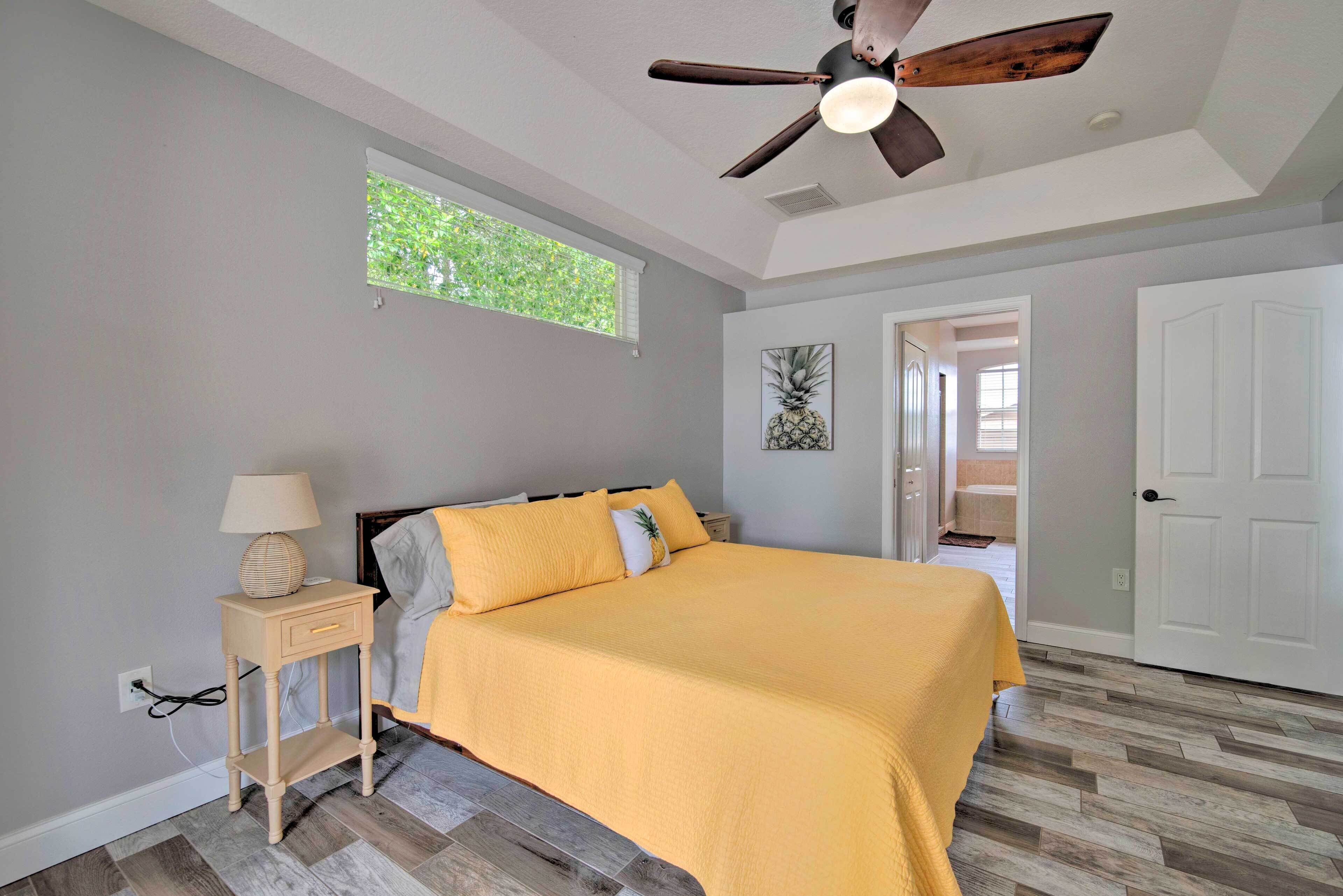 A bedroom with a bed, a nightstand, a ceiling fan, a window, and a door.