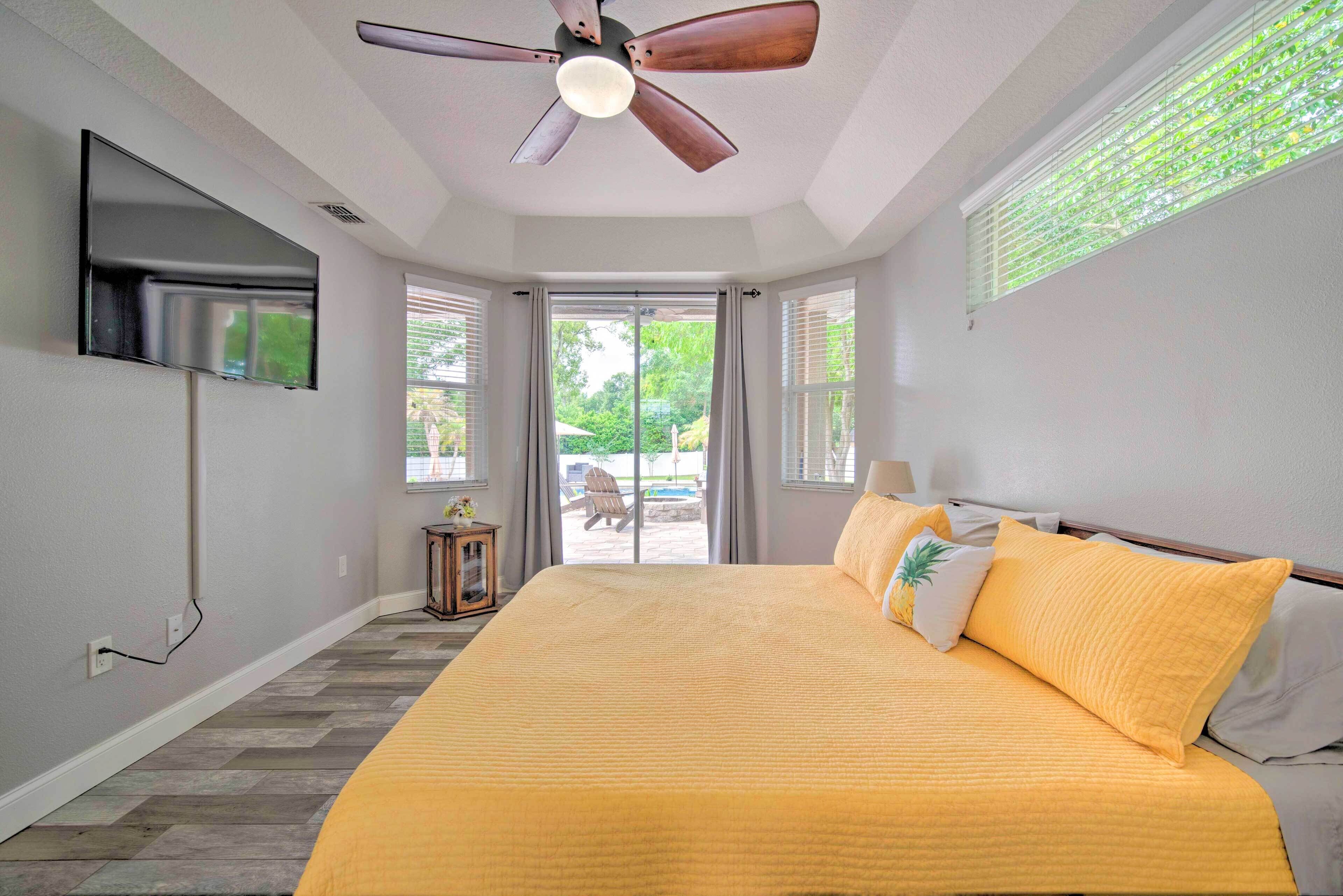 A bedroom with a large bed, a ceiling fan, and a TV mounted on the wall.