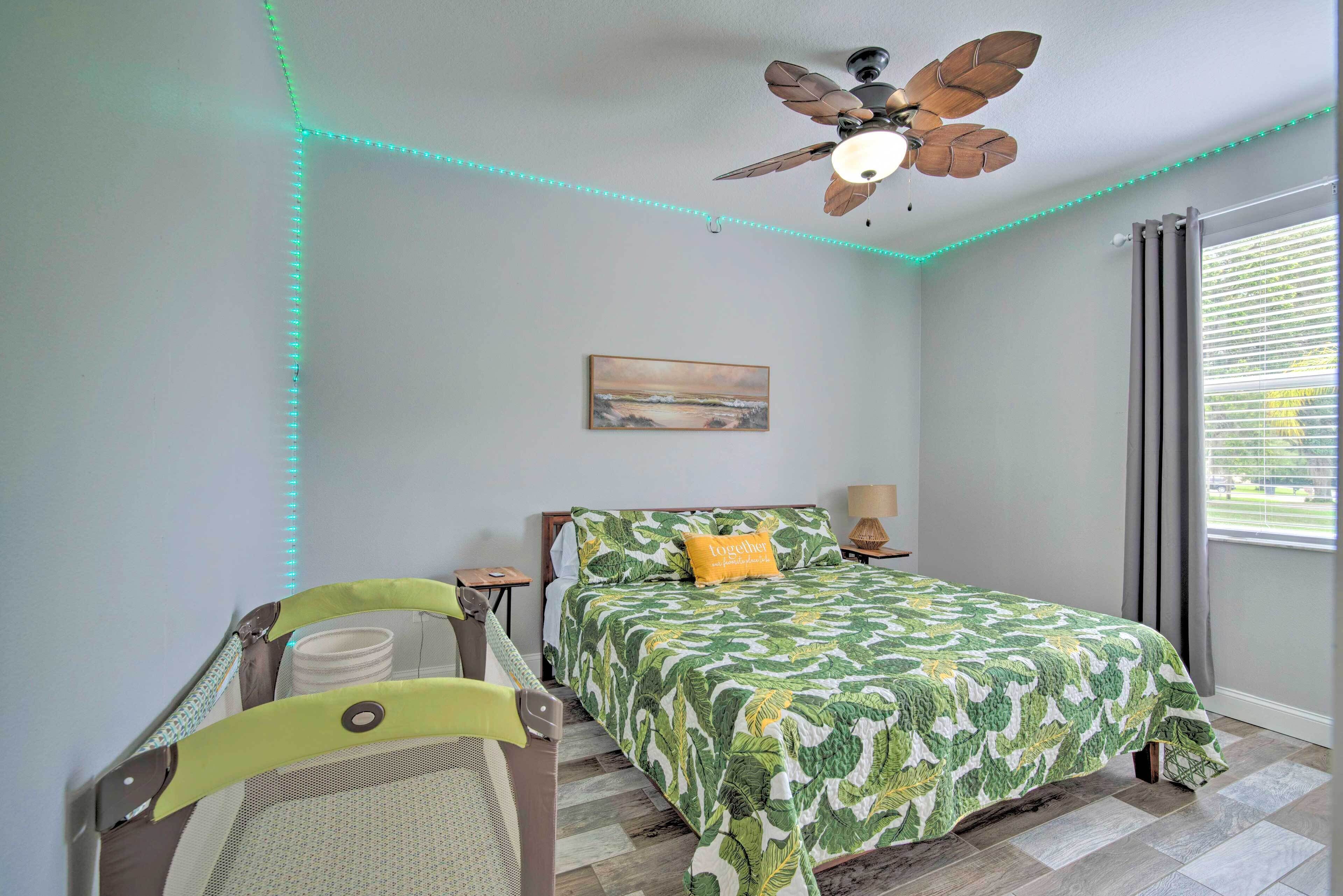 A bedroom with a bed, a ceiling fan, a painting on the wall, and a window with curtains.