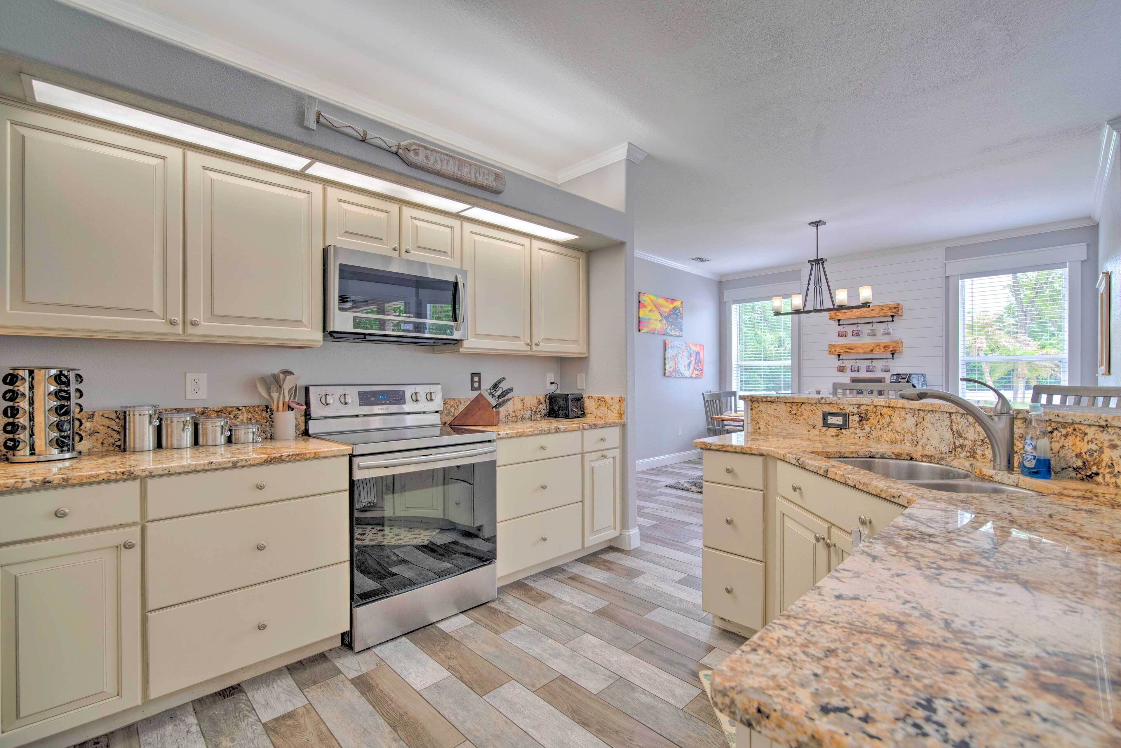 A kitchen with light-colored cabinets, a microwave, an oven, granite countertops, and a window with blinds.