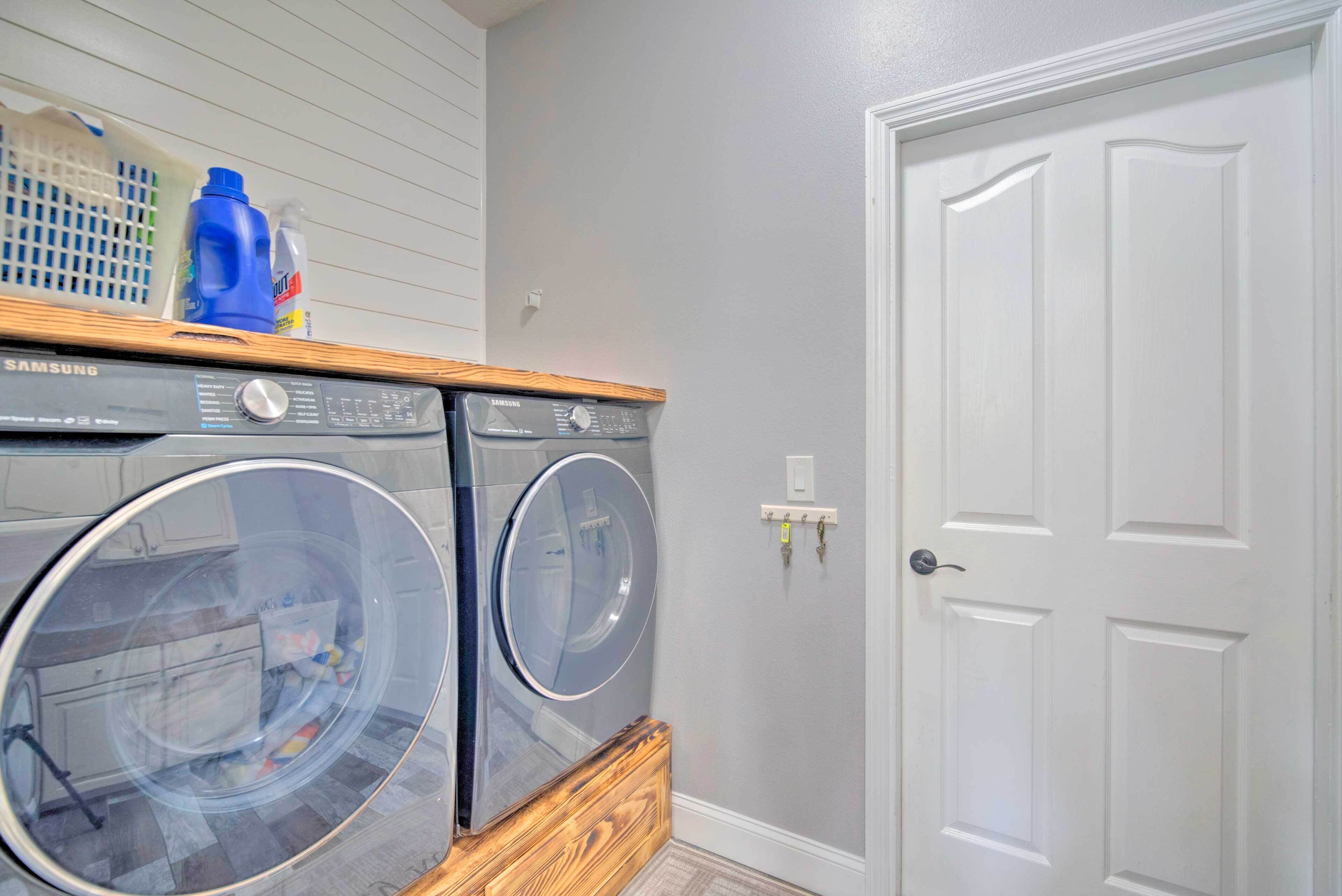 A laundry area with two front-loading washing machines, a wooden shelf with cleaning supplies, and a white door.