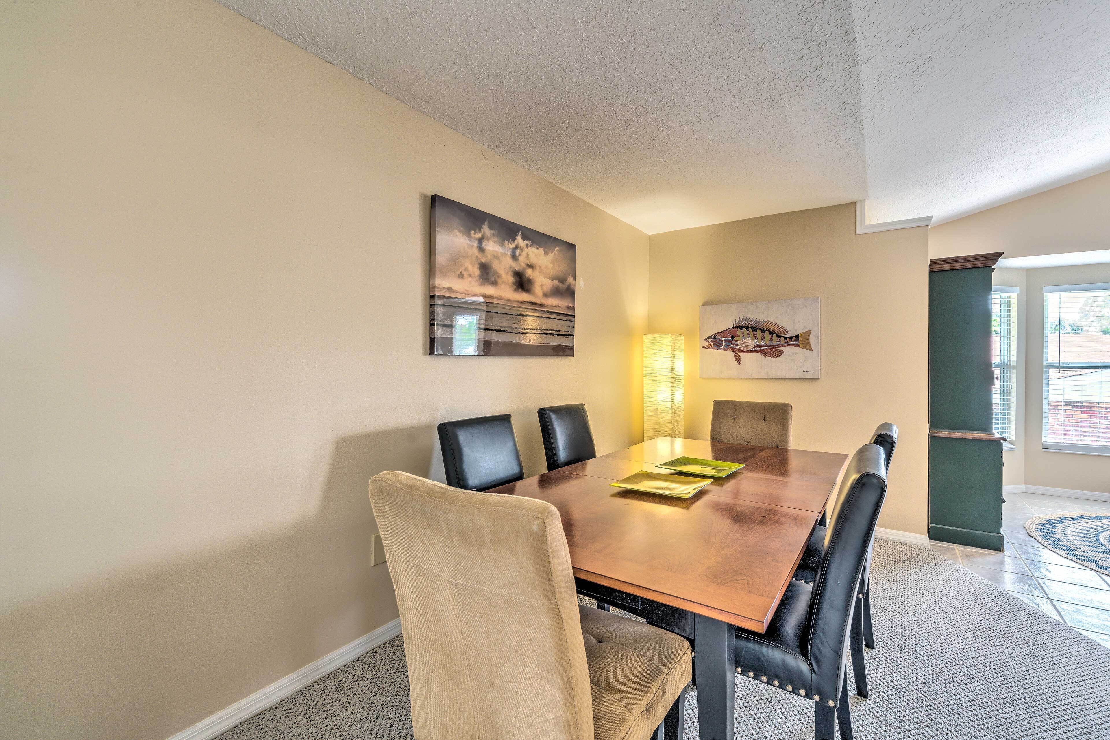 A dining area with a wooden table, six chairs, and artwork on the walls.