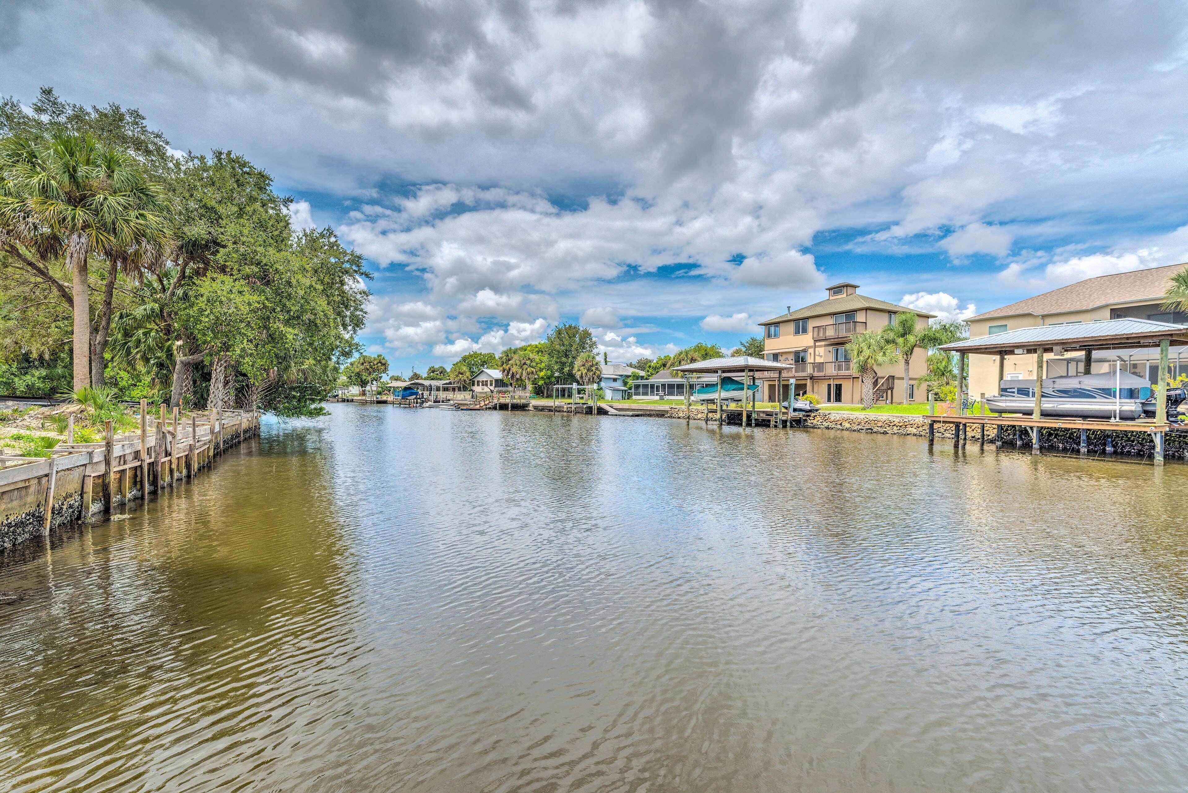 A calm river with a wooden walkway on the left, surrounded by lush greenery and trees.