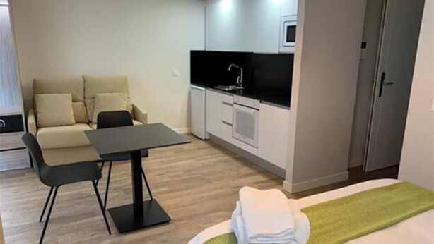 Una habitación de hotel pequeña con cama, una mesita, un sofá, kitchenette y una puerta.