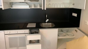 Cocina compacta con estufa, horno y lavaplatos. Hay armarios sobre la encimera y un cajón pequeño debajo.