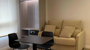 Una sala moderna con un sofá, dos sillas negras, una mesa y una lámpara colgante.