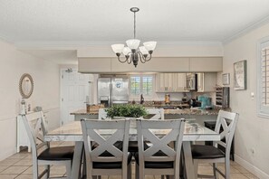 A kitchen with a central island, white cabinetry, a chandelier, and a dining area with a marble table and chairs. - Miramar Beach Retreat - Beachfront & Poolside (Miramar Beach)