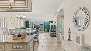 A kitchen with a marble countertop, a dining area with a table and chairs, a large mirror, and a view through a glass door. - Miramar Beach Retreat - Beachfront & Poolside (Miramar Beach)