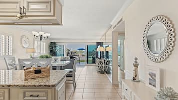 A kitchen with a marble countertop, a dining area with a table and chairs, a large mirror, and a view through a glass door.