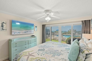 Quarto com cama, ventoinha no teto, televisão e vista para a piscina e área externa.