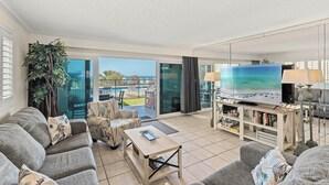 A spacious living room with a large TV, comfortable seating, a coffee table, and a view of a pool and outdoor area. - Miramar Beach Retreat - Beachfront & Poolside (Miramar Beach)
