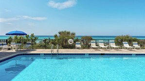 A pool with clear blue water, surrounded by lounge chairs and a blue umbrella, with a view of the ocean. - Miramar Beach Retreat - Beachfront & Poolside (Miramar Beach)