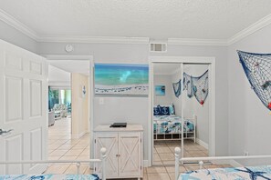 A bedroom with a bed, a small cabinet, a painting of a beach, and a net decoration on the wall. - Miramar Beach Retreat - Beachfront & Poolside (Miramar Beach)
