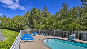 Ein Swimmingpool mit blauen Liegestühlen und einem überdachten Bereich, umgeben von einem weißen Zaun und Bäumen.