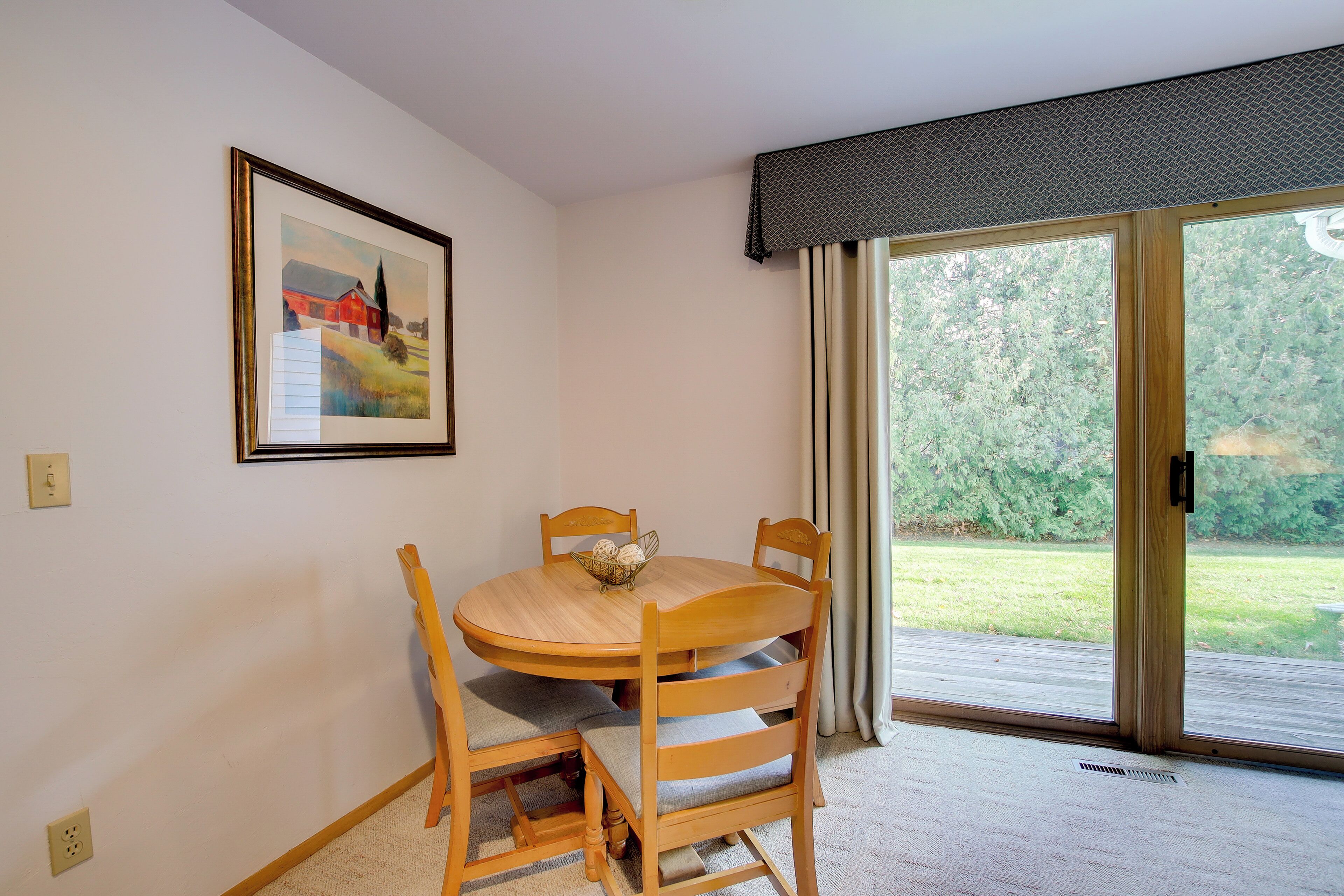 Ein Essbereich mit Holztisch und -stühlen, einem gerahmten Bild an der Wand und einer Glasschiebetür, die zu einem Garten führt.