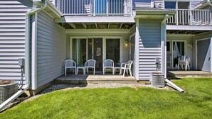 Ein zweistöckiges Haus mit einer überdachten Terrasse, Sitzgelegenheiten im Freien und einem kleinen Garten.