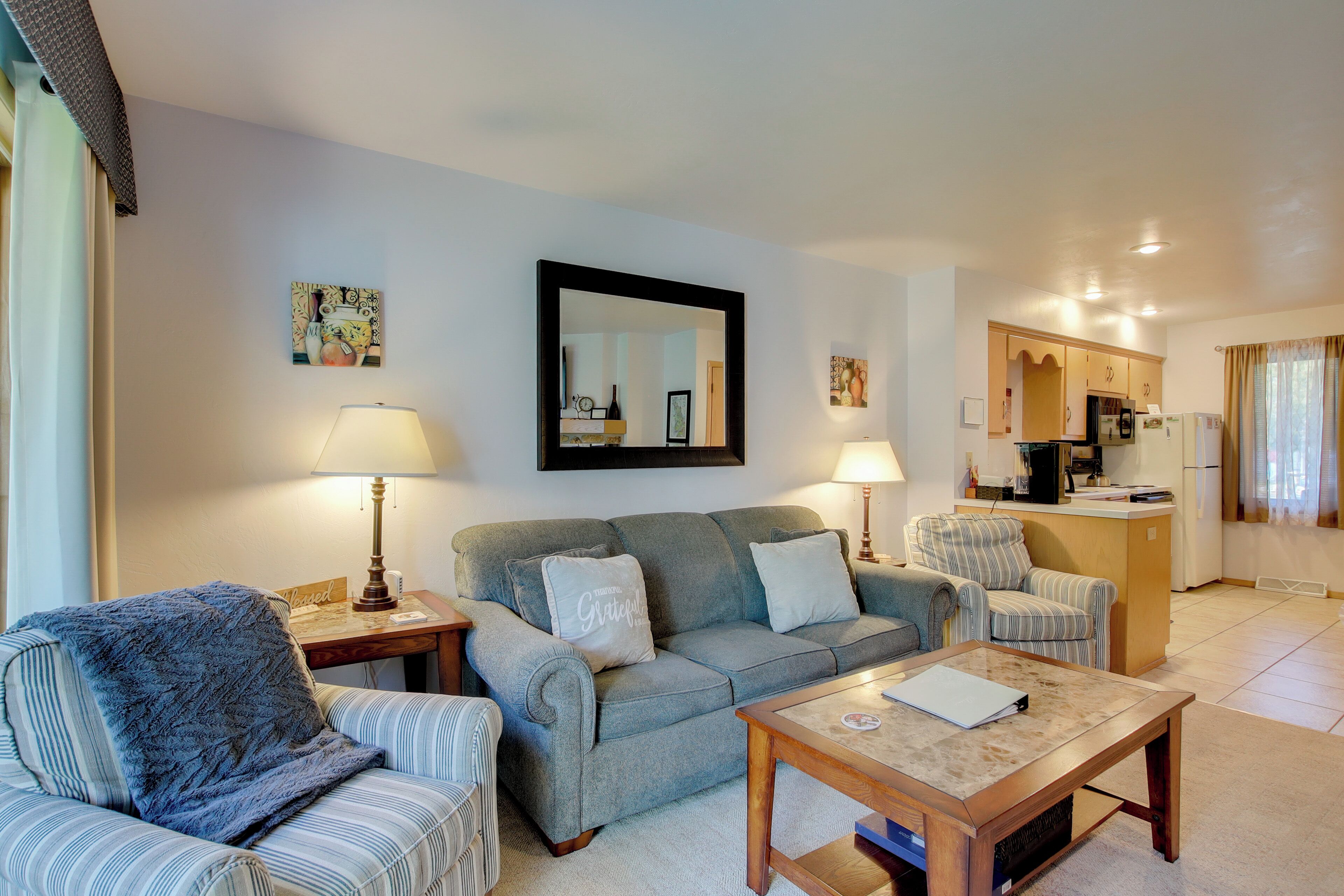 A living room with a sofa, armchairs, a coffee table, and a kitchen in the background.