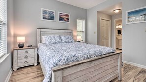 Une chambre à coucher avec un lit en bois, deux tables de chevet avec des lampes, une petite table et une porte donnant sur une salle de bain.