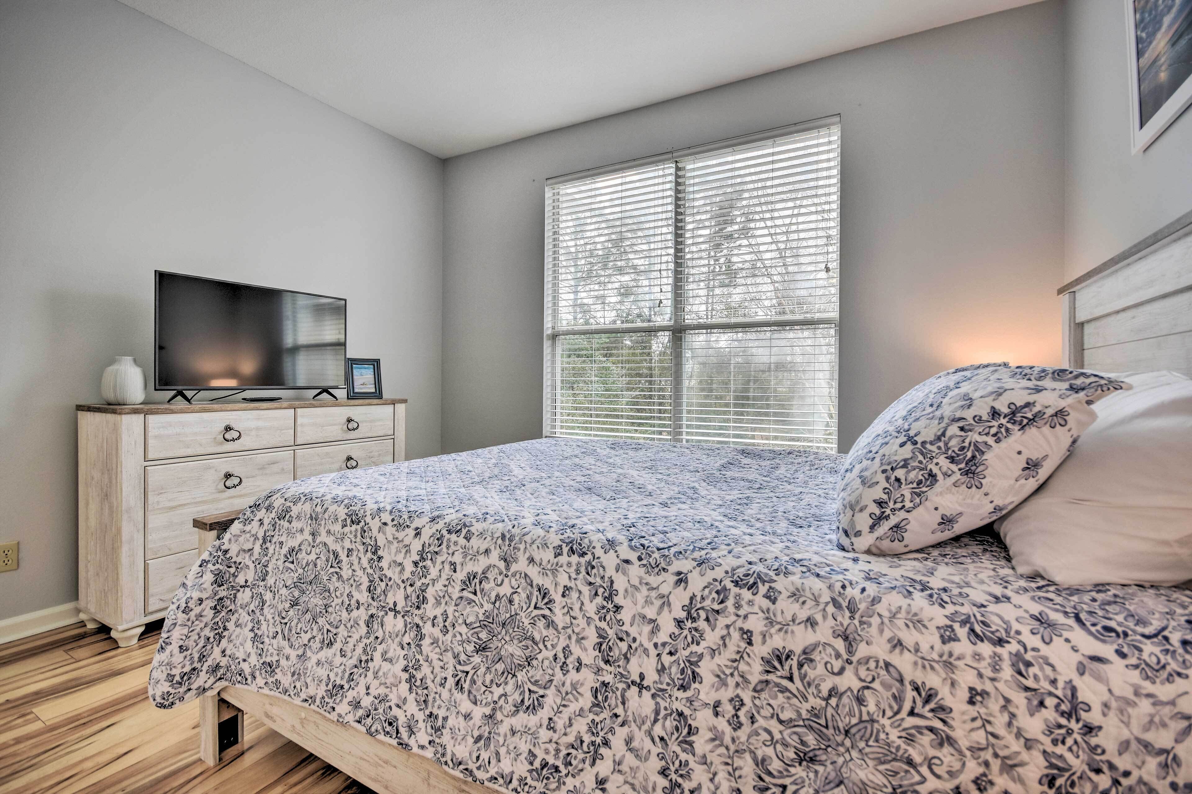 Un dormitorio con cama, cómoda, televisor y ventana con persianas.