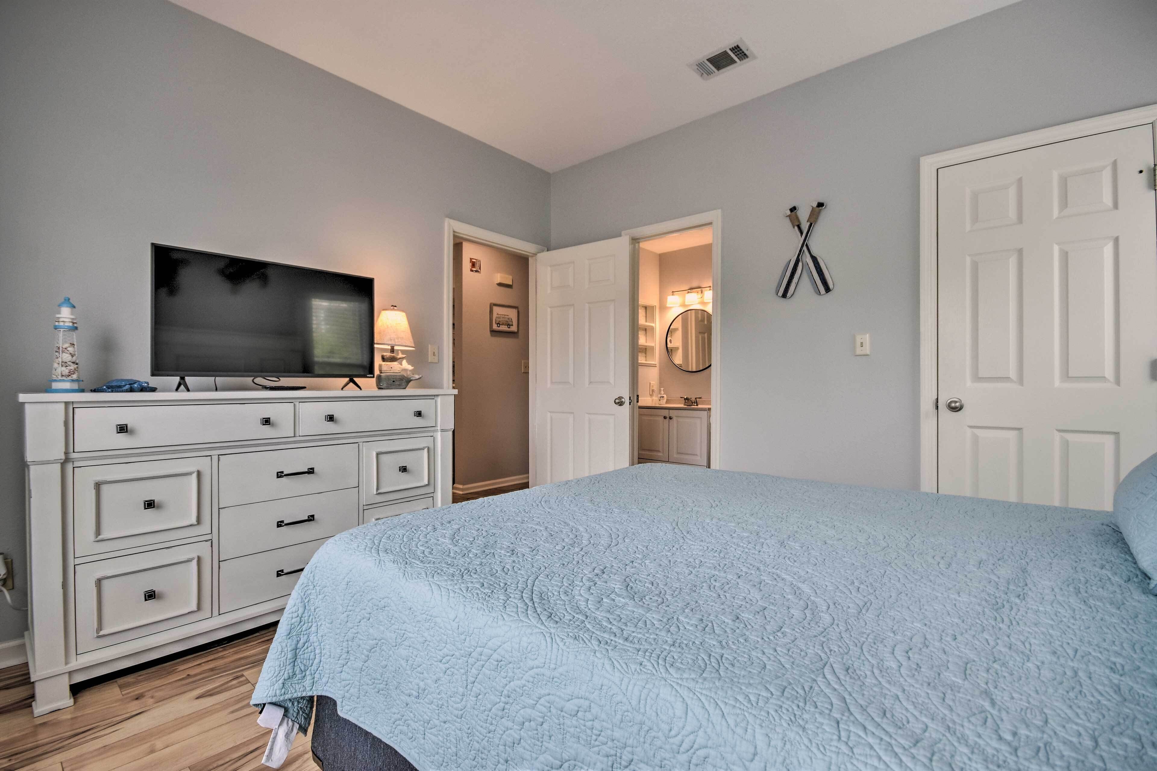 A bedroom with a bed, a dresser, a TV, and a bathroom visible through an open door.