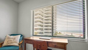 A corner room with a wooden desk, a teal chair, and a window with blinds. - Oceanfront Daytona Beach Condo w/ Beach Views! (Daytona Beach)