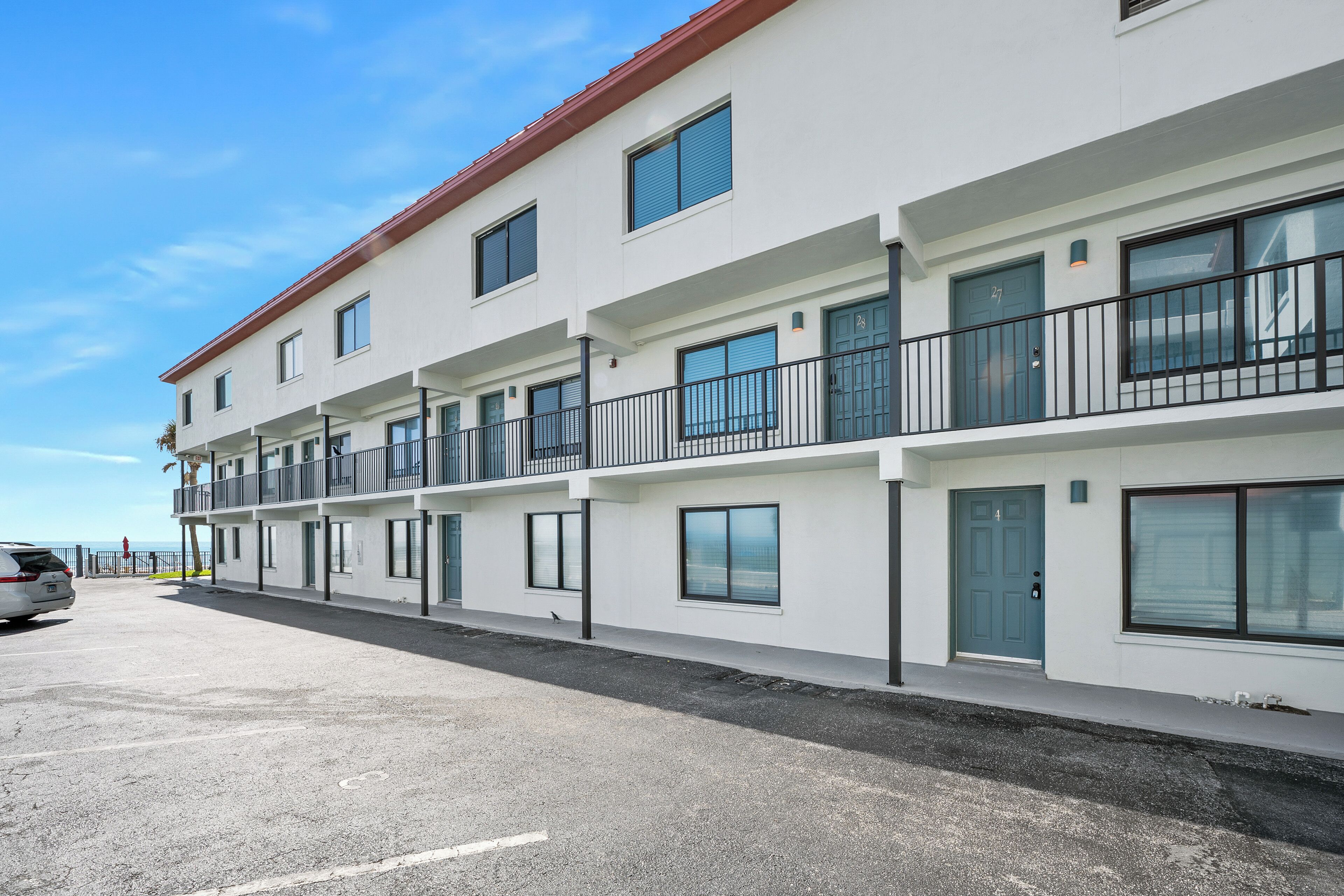 A modern multi-story building with balconies, large windows, and a parking area.