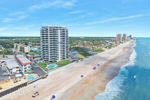 A beachfront hotel with a large building, a sandy beach, and the ocean.