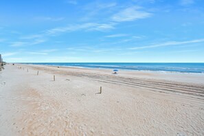 A wide, sandy beach with a clear blue sky and calm sea.