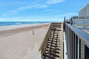 A beach view with a wooden deck and a building with balconies.