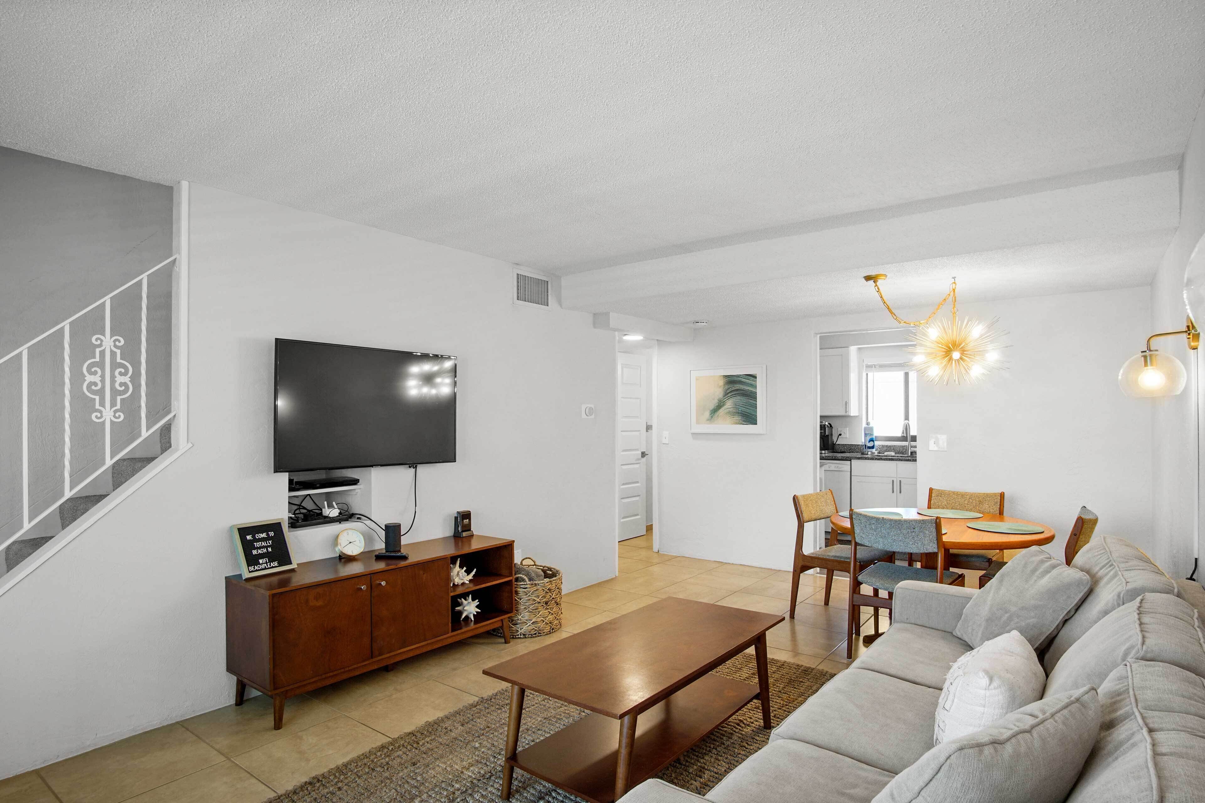 A modern living room with a flat-screen TV, a wooden cabinet, a sofa, and a dining area with chairs and a table.