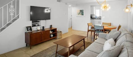 A modern living room with a flat-screen TV, a wooden cabinet, a sofa, and a dining area with chairs and a table.