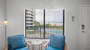A room with a view of a pool and buildings, a white door, and a small table with a chair. - Oceanfront Daytona Beach Condo w/ Beach Views! (Daytona Beach)