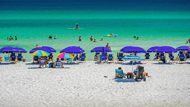 A beach with multiple sun umbrellas and lounge chairs, a clear blue sea, and people swimming and relaxing. - Beachy Lakefront Escape - Walk to the Shore! (Miramar Beach)