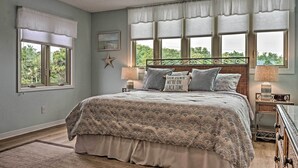 A bedroom with a large bed, two bedside tables, a nightstand, and a window with a view of greenery. - Beachy Lakefront Escape - Walk to the Shore! (Miramar Beach)