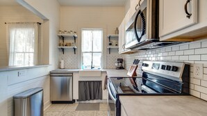 Une cuisine avec des murs recouverts de carreaux blancs, des appareils électroménagers en acier inoxydable et une fenêtre avec un rideau.