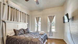Une chambre avec un grand lit, un ventilateur de plafond et un téléviseur à écran plat fixé au mur.