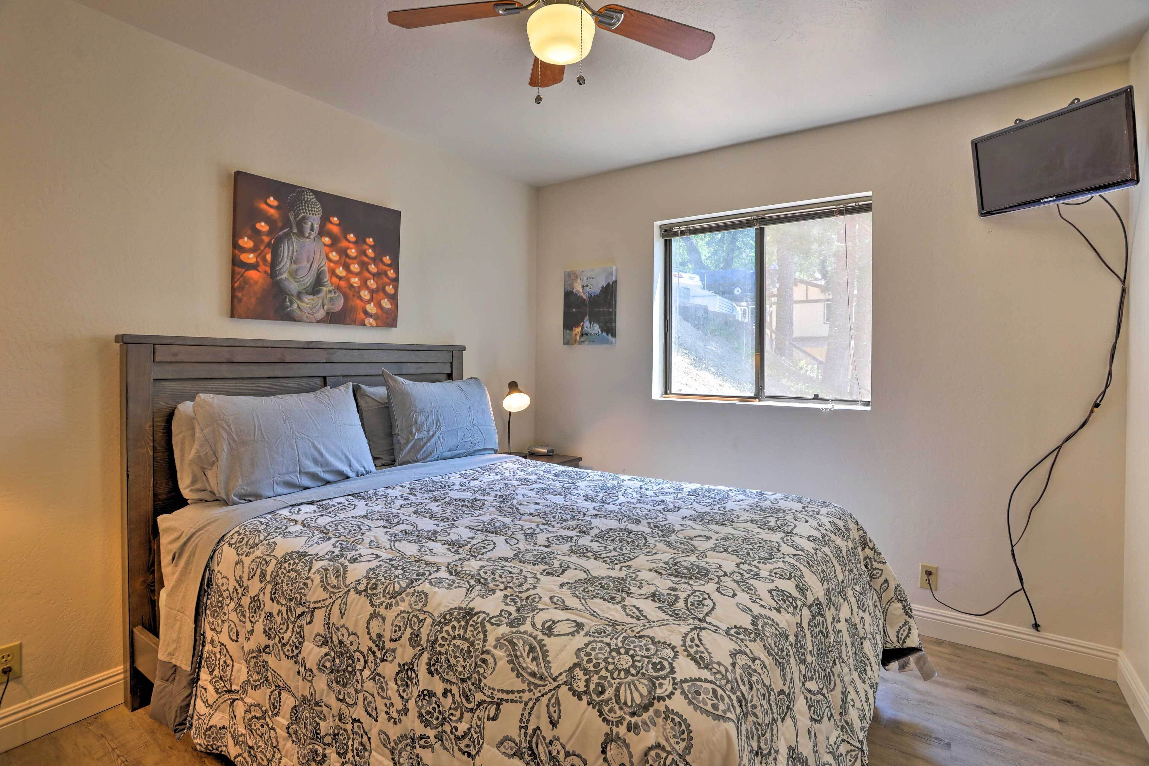 A bedroom with a bed, a ceiling fan, a window, and artwork on the walls.