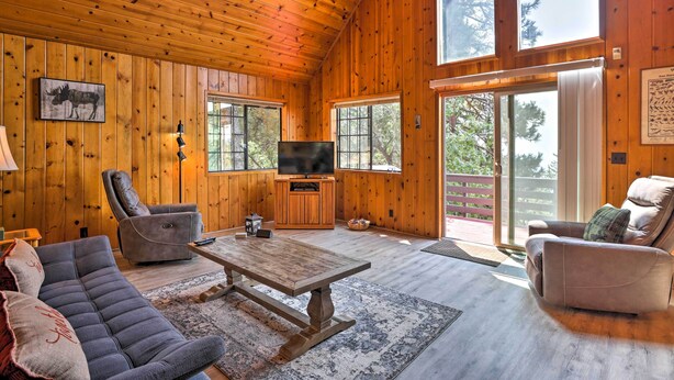Ein Holzblockhaus-Interieur mit Holzbalkendecke, großen Fenstern, einem Fernseher und bequemen Sitzgelegenheiten.