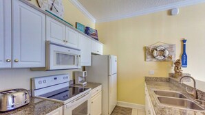 Une cuisine avec des meubles blancs, un four à micro-ondes, un grille-pain, une cuisinière, un réfrigérateur et un évier.