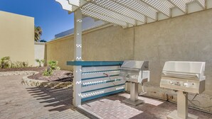 Un espace barbecue extérieur doté d’un gril et d’un coin barbecue, entouré d’une terrasse en briques et d’une pergola.