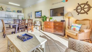 Un salon bien éclairé comprenant un coin repas, des meubles en bois, un téléviseur et une décoration sur le thème de la marine.