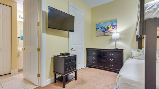 Une chambre à coucher avec un lit, une commode, un téléviseur et un tableau accroché au mur.