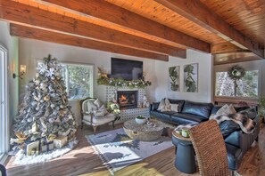 A cozy living room with a fireplace, a Christmas tree, and a leather sofa. - Picturesque Cabin: 2 Balconies, Walk to Lake! (Crestline)