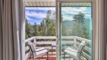 A balcony with two chairs and a wooden deck, overlooking a forested area.