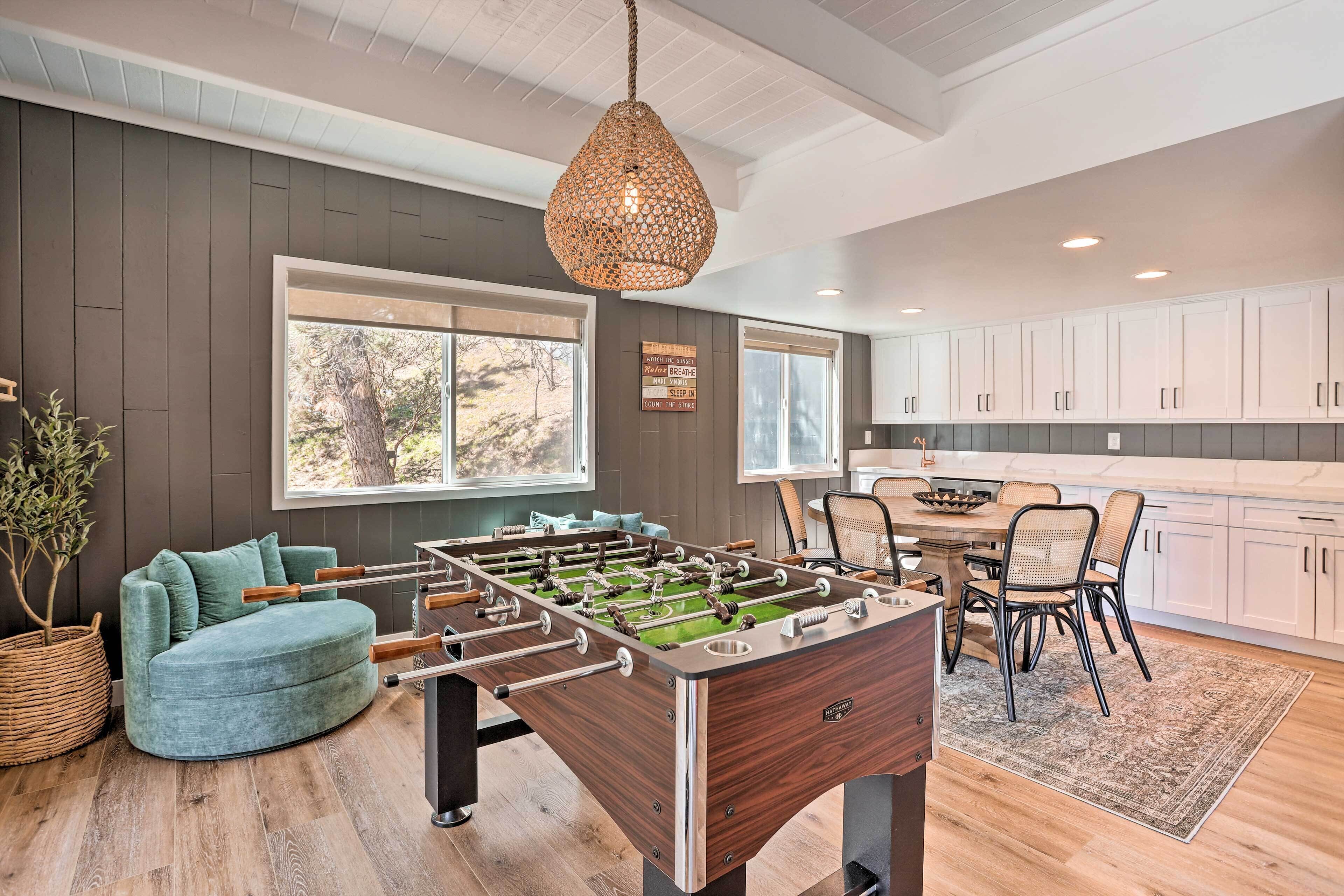 Una cocina moderna con mesa de futbolín, comedor con sillas y un amplio ventanal con vistas al exterior.