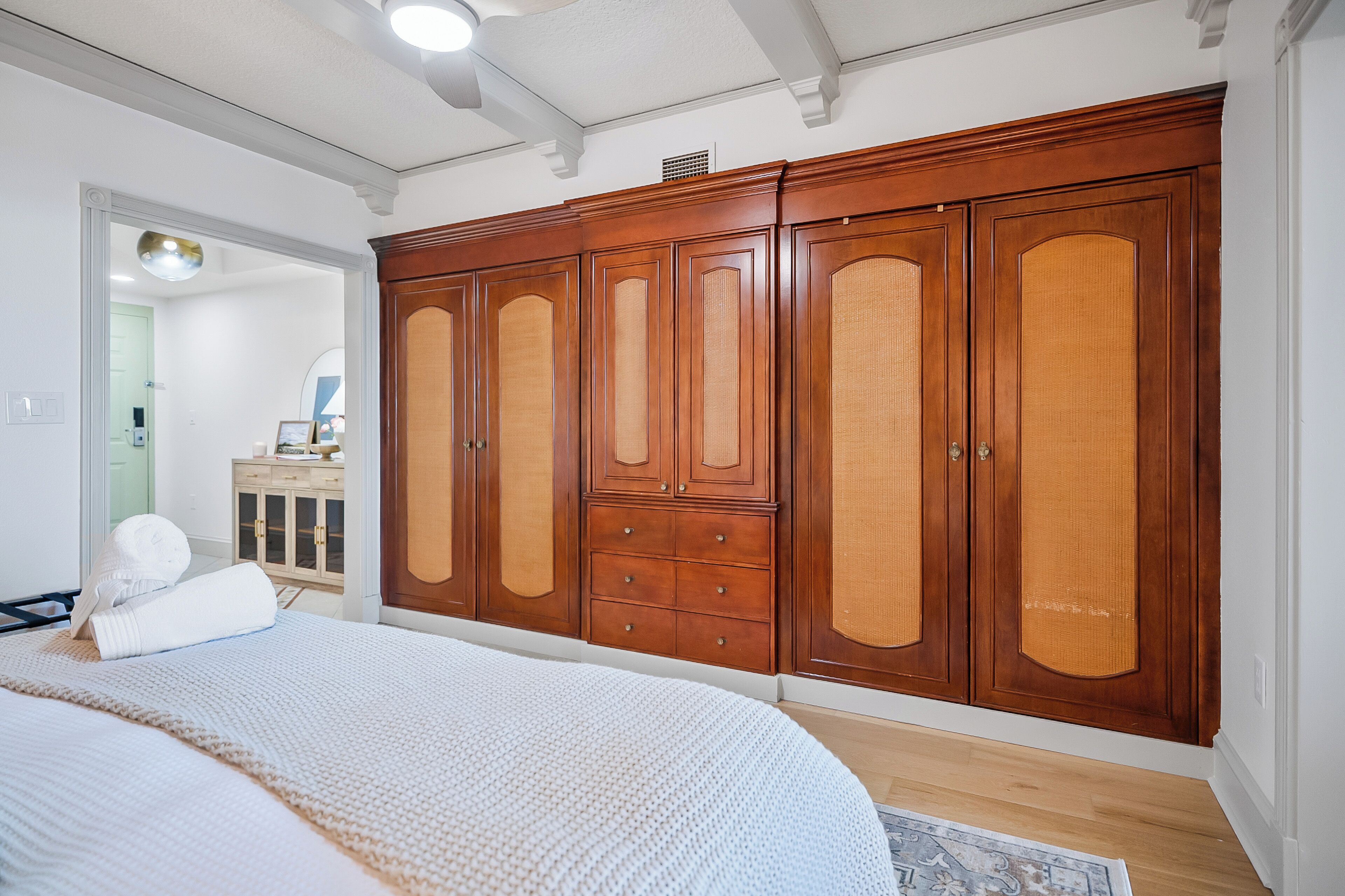 A bedroom with a large wooden wardrobe, a bed with a white blanket, and a wooden floor.
