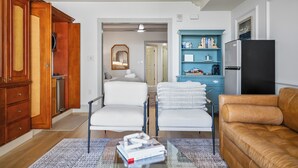 A living room with a sofa, two armchairs, a coffee table with books, a blue shelving unit, and a black refrigerator. - Sunny Hammock Beach Condo: Balcony w/ Ocean Views! (Palm Coast)