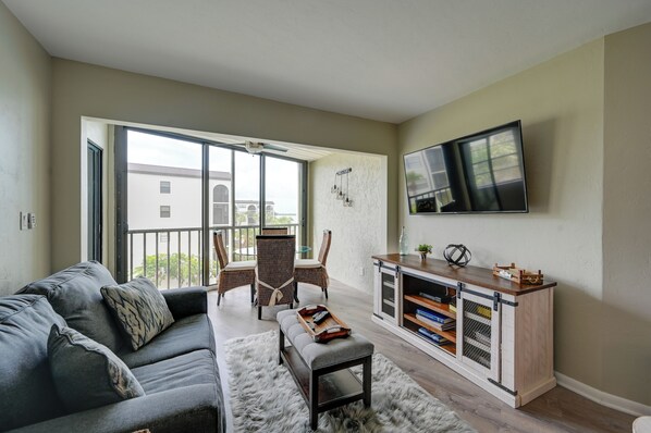 A living room with a grey sofa, a white furry rug, a wooden entertainment unit, and a TV mounted on the wall. - Waterfront Marco Island Condo Near Tigertail Beach (Marco Island)