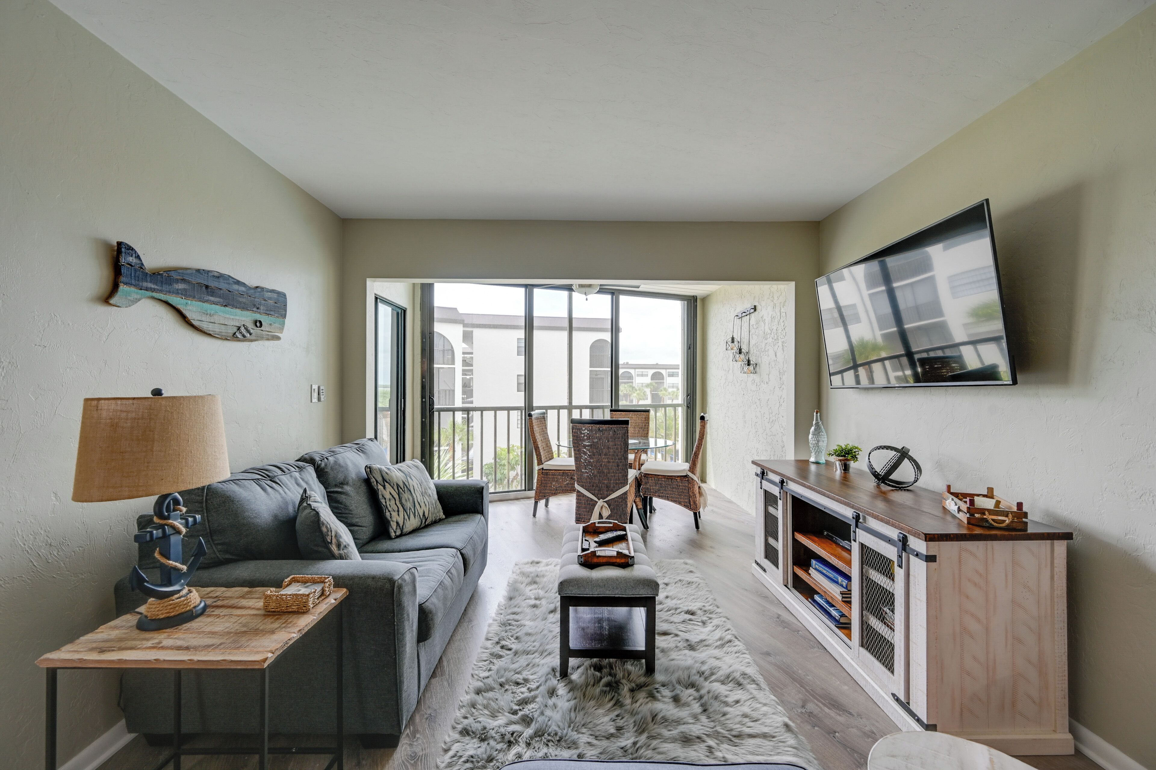 A modern living room with a grey sofa, a wooden coffee table, a fluffy rug, and a dining area with wicker chairs.
